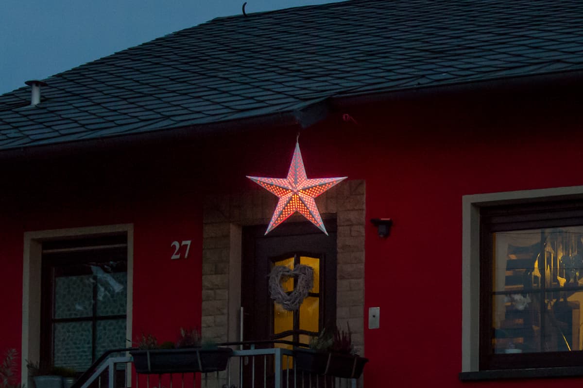 Rot leuchtender Stern über einer Haustür bei Dämmerung